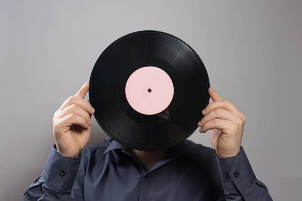 A man in a shirt holds an old vintage vinyl record instead of his head. The idea of a love of antiques.