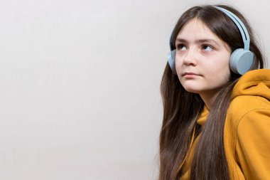 Üzgün bir ergen kız, 12-13 yaşlarında, kulaklık takmış, beyaz arka plan fotokopi odasında mesaj atmak için oturuyor. Ergenlik sorunları, yalnızlık, okulda zorbalık..