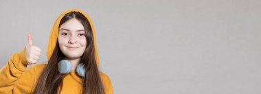 Kafasında parlak kapüşonlu sweatshirt ve kulaklığı olan genç bir kız parmağını havaya kaldırıyor. İnternetten öğrenmek, uzaktan eğitim almak. Hafif bir arkaplanda, metin için alanı kopyala.