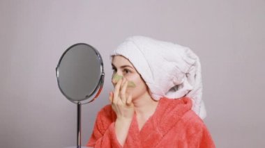 Pembe bornozlu genç kadın yüzüne Ubtan Ayurvedic karışımı sürüp yüz masajı yapıyor. Yüz ovma ve soyma