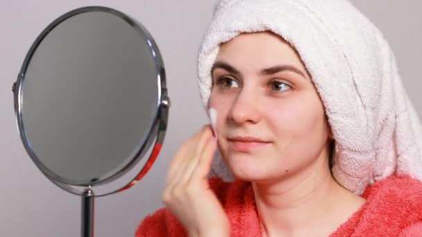 Una giovane donna in vestaglia rosa applica una schiuma per pulire la pelle. Detergere la pelle del viso da impurità, sebo, prevenzione di punti neri e acne — Video Stock