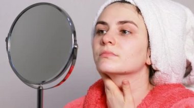 Pembe bornozlu genç bir kadın yüz masajı yapıyor, kafasından beyaz bir havlu düşüyor. Kozmetolojide cilt bakımı hakkında komik bir video.