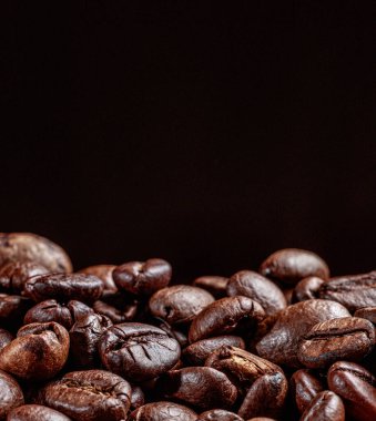 Siyah arka planda kahve çekirdeklerinin nefes kesici bir fotoğrafı. Reklam için metin ya da kahve dükkanı için önerisi olan dikey afiş.