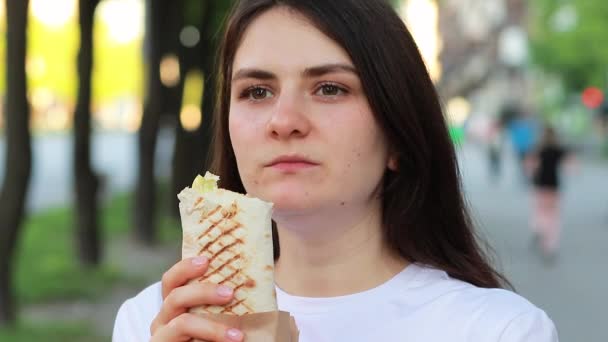 En vacker kvinna äter shawarma på en stadsgata. Snabbmat på väg till jobbet eller skolan. — Stockvideo