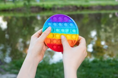 Renkli bir oyuncak doğadaki bir gölün arka planındaki bir yetişkinin ellerine bırak. Stres önleyici oyuncak ya da tekrar kullanılabilir köpük ambalajı. 2021 Trend