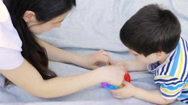 Mamá y bebé niño de 4 años juegan con un juguete de moda de color Pop en el parque en la naturaleza. Juguete sensible al estrés o envoltura de burbuja reutilizable. Tendencia de 2021. — Vídeos de Stock