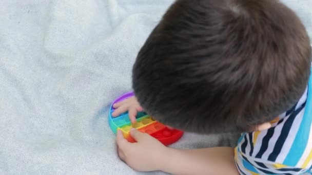 Un petit garçon de 4 ans joue avec Pop It dans la nature. Jouet anti-stress pour le développement de la motricité fine chez les enfants. — Video