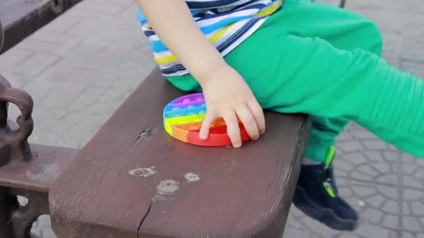 Ett barn på 4 år leker med Pop It i stadsparken. Antistress leksak för utveckling av finmotorik hos barn. — Stockvideo