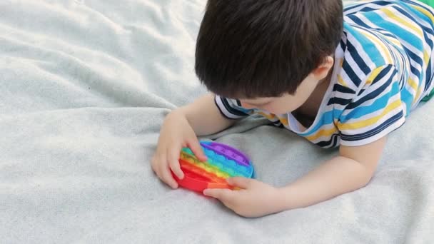 Um menino de 4 anos brinca com Pop It na natureza. Brinquedo anti-stress para o desenvolvimento de habilidades motoras finas em crianças. — Vídeo de Stock