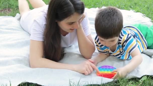 Μαμά και το αγοράκι 4 ετών παίζουν με ένα έγχρωμο μοντέρνο παιχνίδι Pop στο πάρκο στη φύση. Αντιστρες ευαίσθητο παιχνίδι ή επαναχρησιμοποιήσιμο περιτύλιγμα φυσαλίδων. Τάση 2021. — Αρχείο Βίντεο