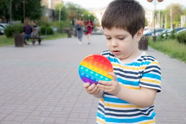Un niño de 4 años juega con Pop It en el parque de la ciudad. Juguete antiestrés para el desarrollo de habilidades motoras finas en niños. — Foto de Stock
