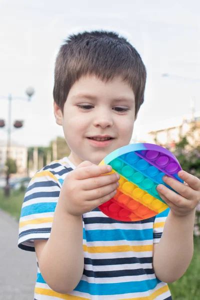 Un niño juega con Pop It en el parque de la ciudad. Juguete antiestrés para el desarrollo de habilidades motoras finas en niños. Foto vertical. — Foto de Stock