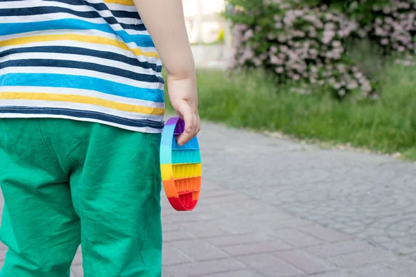 Un niño pequeño sostiene un juguete antiestrés pop con un lugar para el texto en el fondo del parque de la ciudad. — Foto de Stock