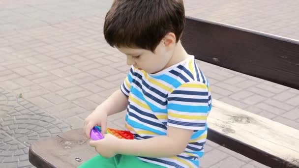 4 yaşında bir çocuk Pop It ile şehir parkında oynuyor. Çocuklarda iyi motor becerileri geliştirmek için stres önleyici oyuncak. — Stok video