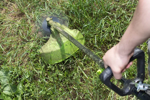 Muž s elektrickou sekačkou seká trávu. Pro zahradnický sklad vybavení. — Stock fotografie