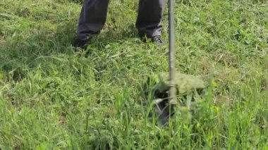 Elektrikli çim biçme makinesi olan bir adam çimleri biçiyor. Çim biçme bıçağı yakın planda dönüyor..