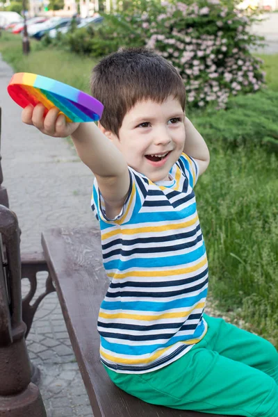 Un niño juega con Pop It en el parque de la ciudad. Juguete antiestrés para el desarrollo de habilidades motoras finas en niños. Foto vertical. — Foto de Stock