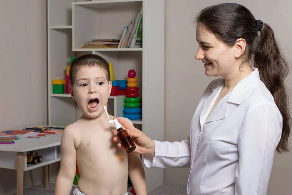 Un pédiatre ou une infirmière et un garçon de 3 à 4 ans. Spray pour la gorge, traitement de la pharyngite, stomatite ou muguet chez l'enfant. — Photo