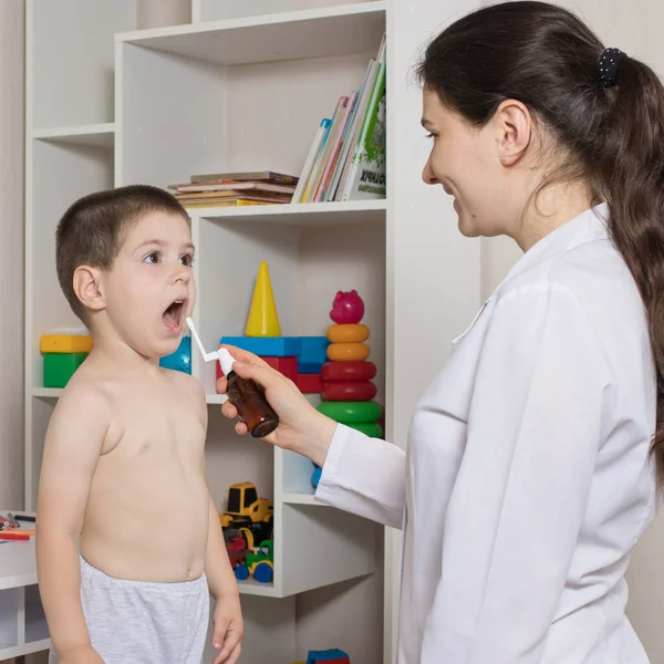 Een kinderarts of verpleegkundige en een jongen van 3-4 jaar oud. Keelspray, behandeling van faryngitis, stomatitis of spruw bij kinderen. — Stockfoto