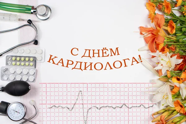 Zdravotní přání s nápisem na ruském překladu: s denním kardiologem. EKG, fonendoskop, tablety, tonometr a květiny — Stock fotografie
