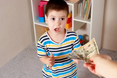 Küçük bir çocuk, yetişkin bir ebeveynin elinden dolarları alıyor. Çocuklarda mali okur yazarlık ve cep harçlığı