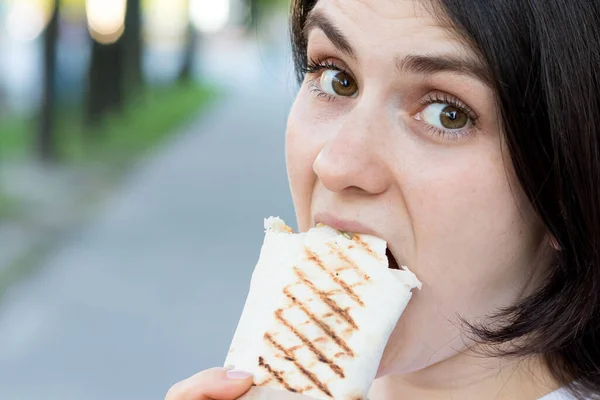Esmer kadın şehir caddesinde çok fazla shawarma yiyor. Et ve sebzeli sokak yemeği Pita 'sı. Metin için yer. — Stok fotoğraf