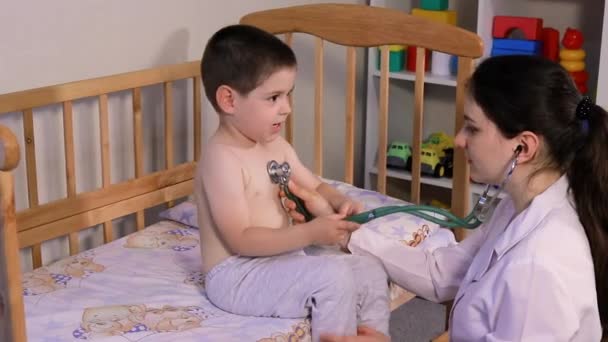 Barnläkaren kommer att auskultulsera lungorna och hjärtat av en liten pojke 3-4 år gammal. Barnmedicin, läkarbesök i hemmet. — Stockvideo
