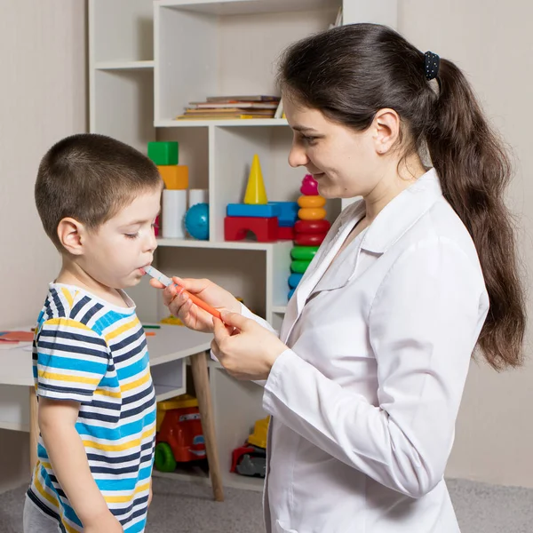 El pediatra o enfermero le da al niño jarabe en una jeringa dosificadora. Tratamiento de la tos, la temperatura en los niños. Paracetamol o ibuprofeno para niños pequeños y preescolares en pediatría — Foto de Stock