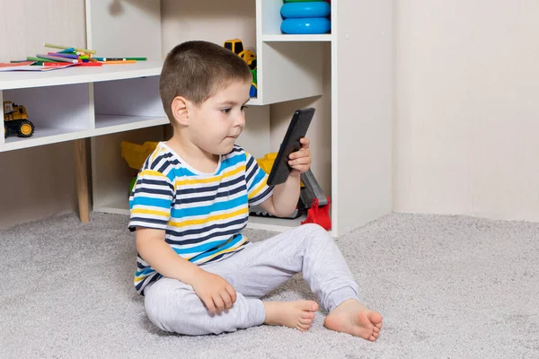 A small child and a mobile phone in the childrens room with place for text. Cartoons and dependence on gadgets in children, limiting children from adult content on the Internet — Stock Photo, Image