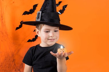 Cadılar Bayramı ve çocuk. Çocuk turuncu arka planda bir balkabağı mumu tutuyor. Metin için alanı kopyala.