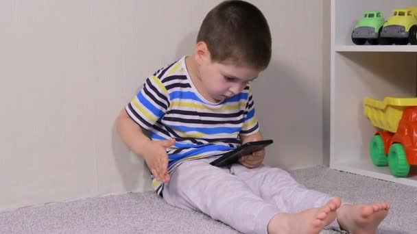 Un petit garçon de 3-4 ans regarde dans l'écran du téléphone. Dessins animés, jeux pour enfants, temps d'écran, dépendance des enfants à l'ordinateur et au téléphone — Video