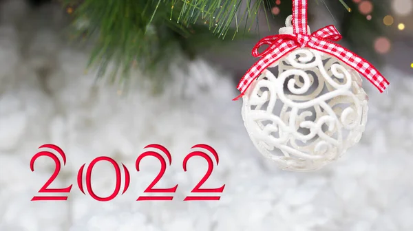 Tarjeta de vacaciones Año Nuevo 2022 banner. Una bola de Navidad blanca y una rama de árbol cubierta de nieve sobre un fondo blanco y nevado. — Foto de Stock