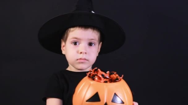 Дитя Хэллоуина. Мальчик в костюме колдуна показывает тыквенное ведро конфет и готовится к празднику. — стоковое видео