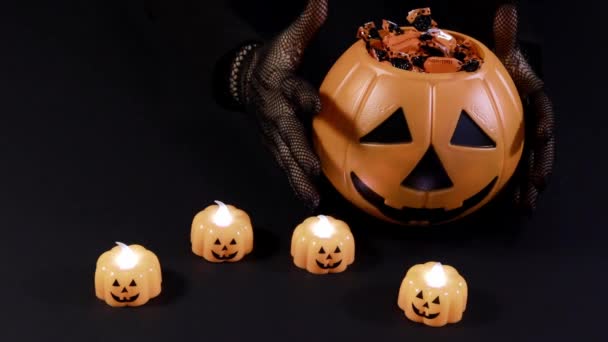 Vorbereitungen für Halloween. Eine Hexe gießt Süßigkeiten aus einem Eimer mit Kürbis auf schwarzem Hintergrund. — Stockvideo