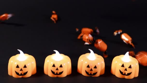 Příprava na Halloween. Pomerančové bonbóny pomalu vylévají na černé pozadí, dýňové lucerny září. — Stock video