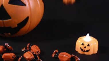 Cadılar Bayramı için hazırlanıyorum. Siyah arka planda balkabakları ve şekerler, balkabakları ön planda yuvarlanıyor.