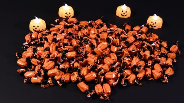 Una mujer en un disfraz de bruja rastrillos puñados de dulces con la inscripción Halloween sobre un fondo negro con velas de calabaza. Preparación para las vacaciones. — Vídeo de stock