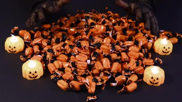 Pregătirea pentru Halloween - o vrăjitoare atinge bomboane portocalii cu mâinile în mănuși de plasă pe fundalul lumânărilor de dovleac pe negru — Videoclip de stoc