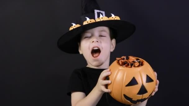 Egy halloweeni gyerek tart egy tököt cukorkával és sikoltozással, dalokat énekel. Felkészülés a nyaralásra — Stock videók