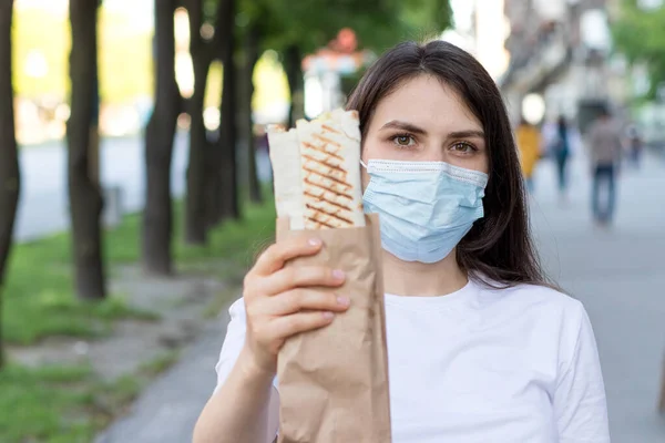 Una repartidora enmascarada tiene un pedido: comida rápida, comida callejera y entrega a domicilio por mensajero durante una pandemia. — Foto de Stock