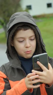 Bir okul çocuğu cep telefonunun ön kamerasına bakarak bir selfie çeker ve yüzünü buruşturur.