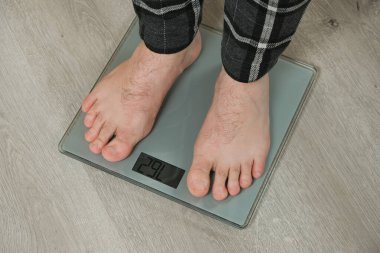 İnsan evdeki modern tartı terazisiyle kendini tartıyor, çıplak ayakla.