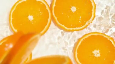 Fresh slices of oranges falling into orange water, splash water, slow motion top view