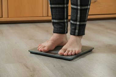İnsan evdeki modern tartı terazisiyle kendini tartıyor, çıplak ayakla.