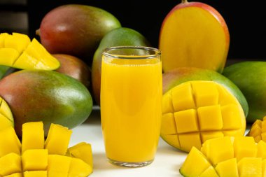 Bir bardak taze mango suyu. Dilimlenmiş meyvelerle çevrili.