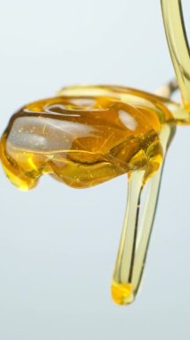 Altın organik bal akışı ve kaşıktan damlayan, dikey ağır çekim