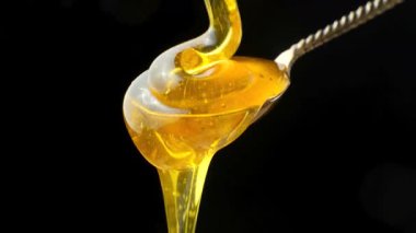 Doğal arı balı kaşığa akıyor ve damlıyor, siyah arka planda makro.