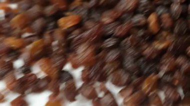 Kahverengi kuru üzüm yığını beyaz arka planda yavaş çekimde dağılmış..