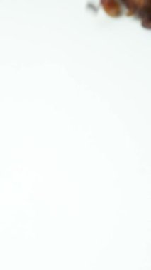 Kahverengi kuru üzüm yığını beyaz arka planda yavaş çekimde dağılmış..