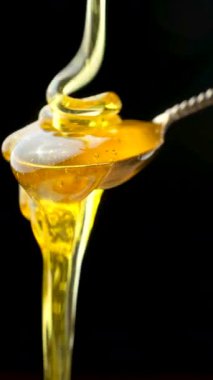 Doğal arı balı kaşığa akıyor ve damlıyor, siyah arka planda makro.